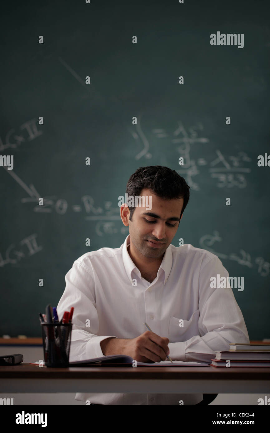 Giovane uomo seduto alla sua scrivania la scrittura con chalk board in background. Foto Stock