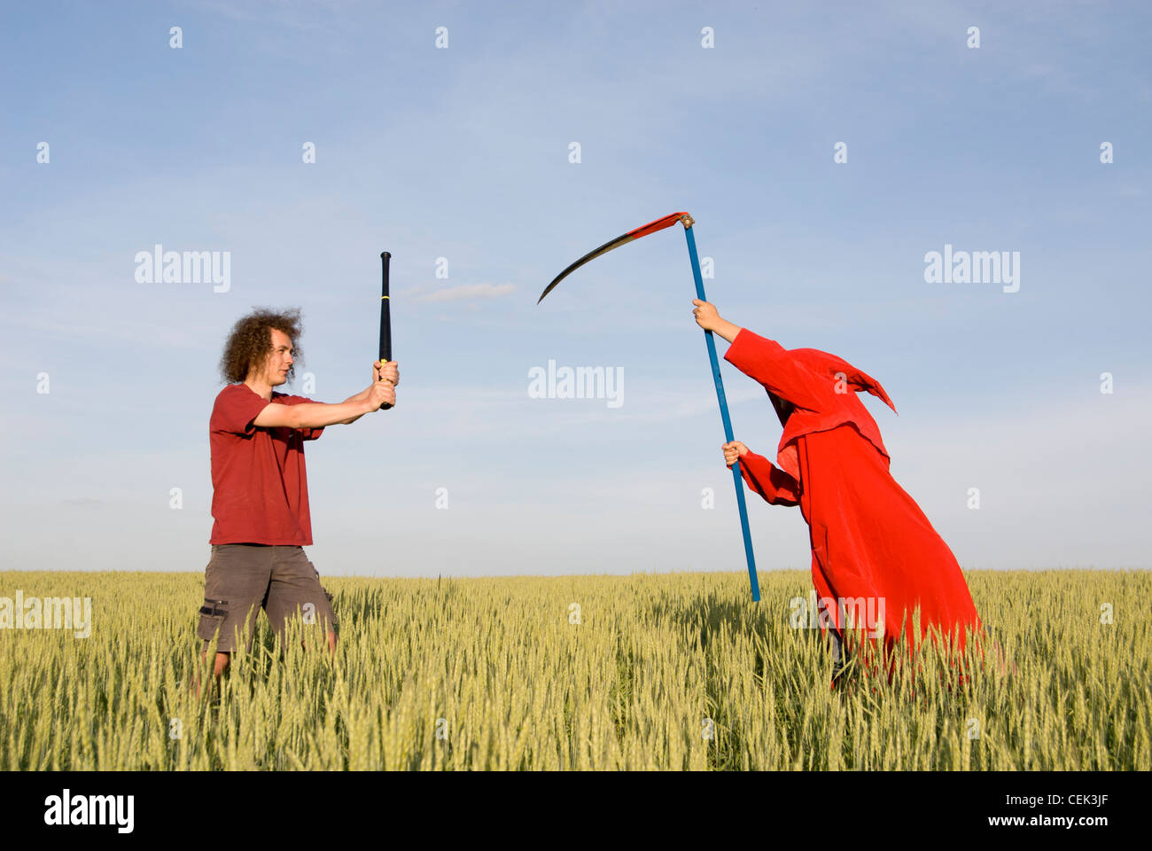 Giovane uomo con la mazza da baseball lottando contro la morte (Grim Reaper) con la falce Foto Stock