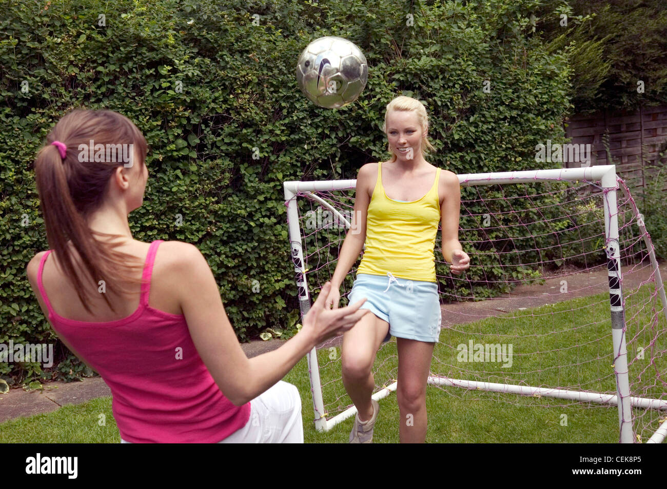 Due femmine a giocare a calcio in giardino entrambe le ginocchia mantenendo sollevato il calcio in aria, vista posteriore della donna sulla sinistra brunette capelli Foto Stock