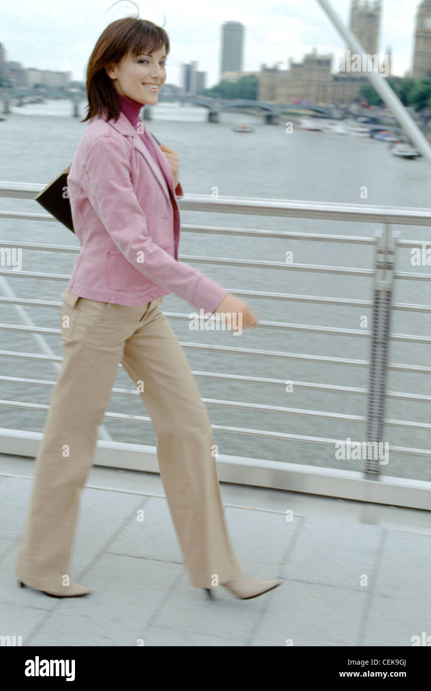 Una femmina di lunghezza di spallamento brunette capelli indossando giacca rosa, rosa scuro collo polo top, beige pantaloni e scarpe beige azienda Foto Stock