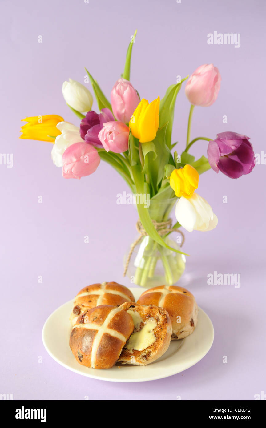 Una vita ancora immagine di un bouquet di tulipani colorati in vaso di vetro legata la corda e tre hot cross panini burro sulla piastra bianca n. Foto Stock