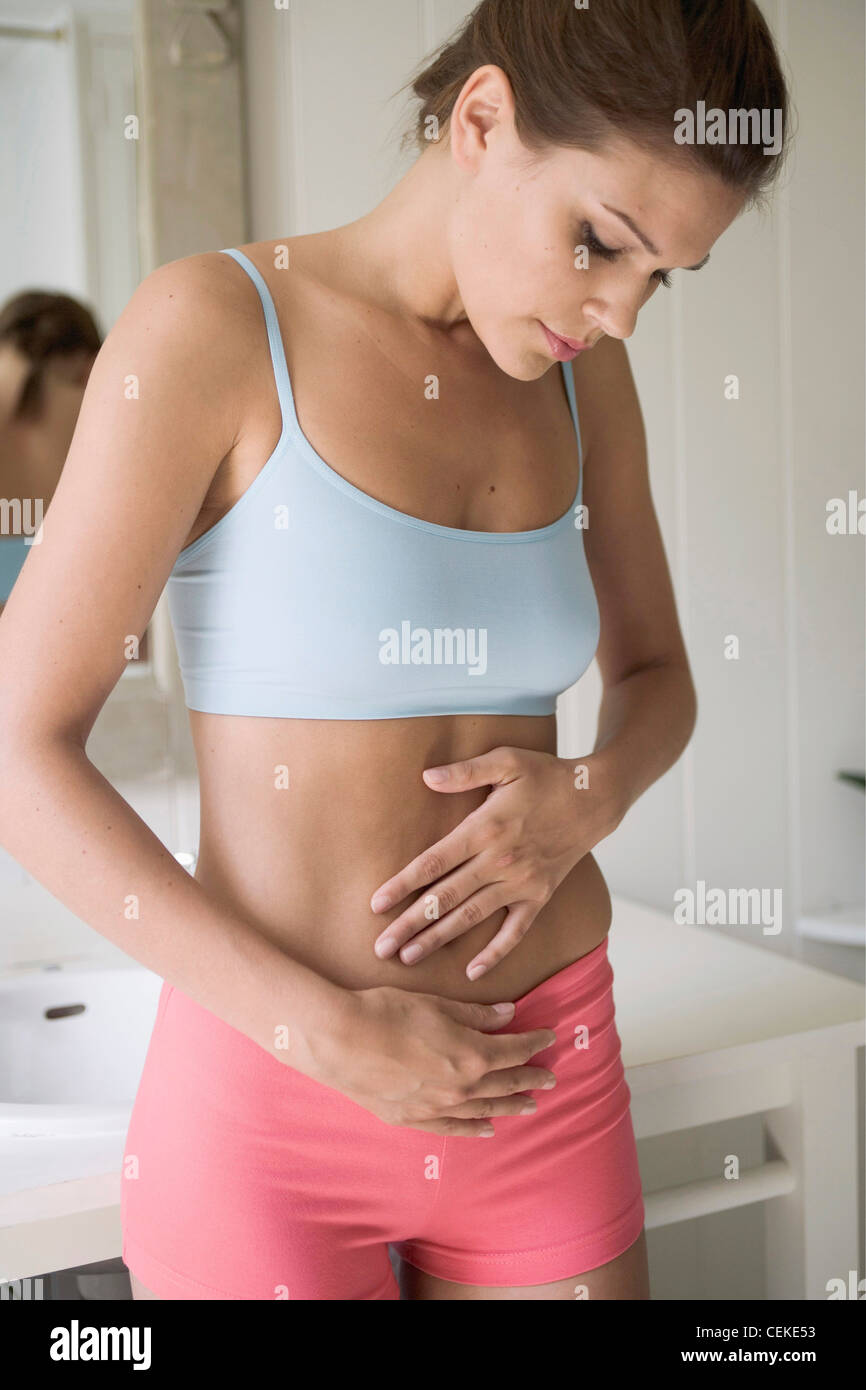 Immagine ritagliata di bruna femmina, indossando un prodotto bianco top e pantaloncini rosa mani su stomaco e guardando verso il basso, c'erano pochi sorrisi Foto Stock