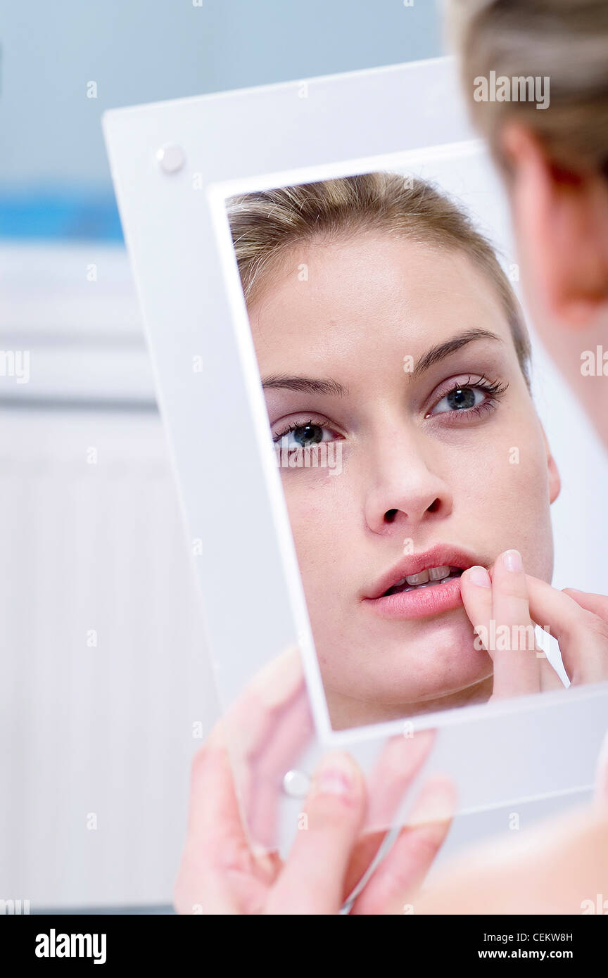 Femmina guardando il suo riflesso in uno specchio, con il dito sull'angolo del suo labbro Foto Stock