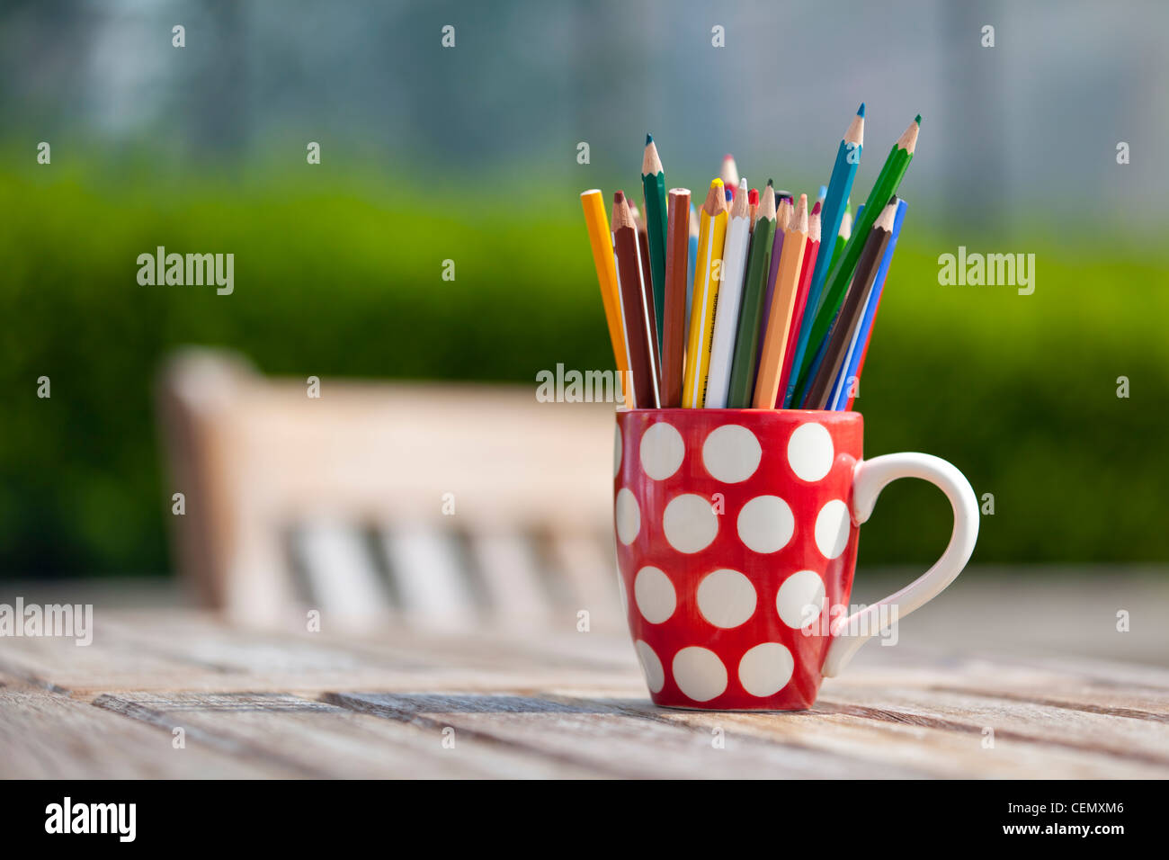 La colorazione di matite colorate in rosso e bianco polka dot mug al di fuori su di un tavolo di legno Foto Stock