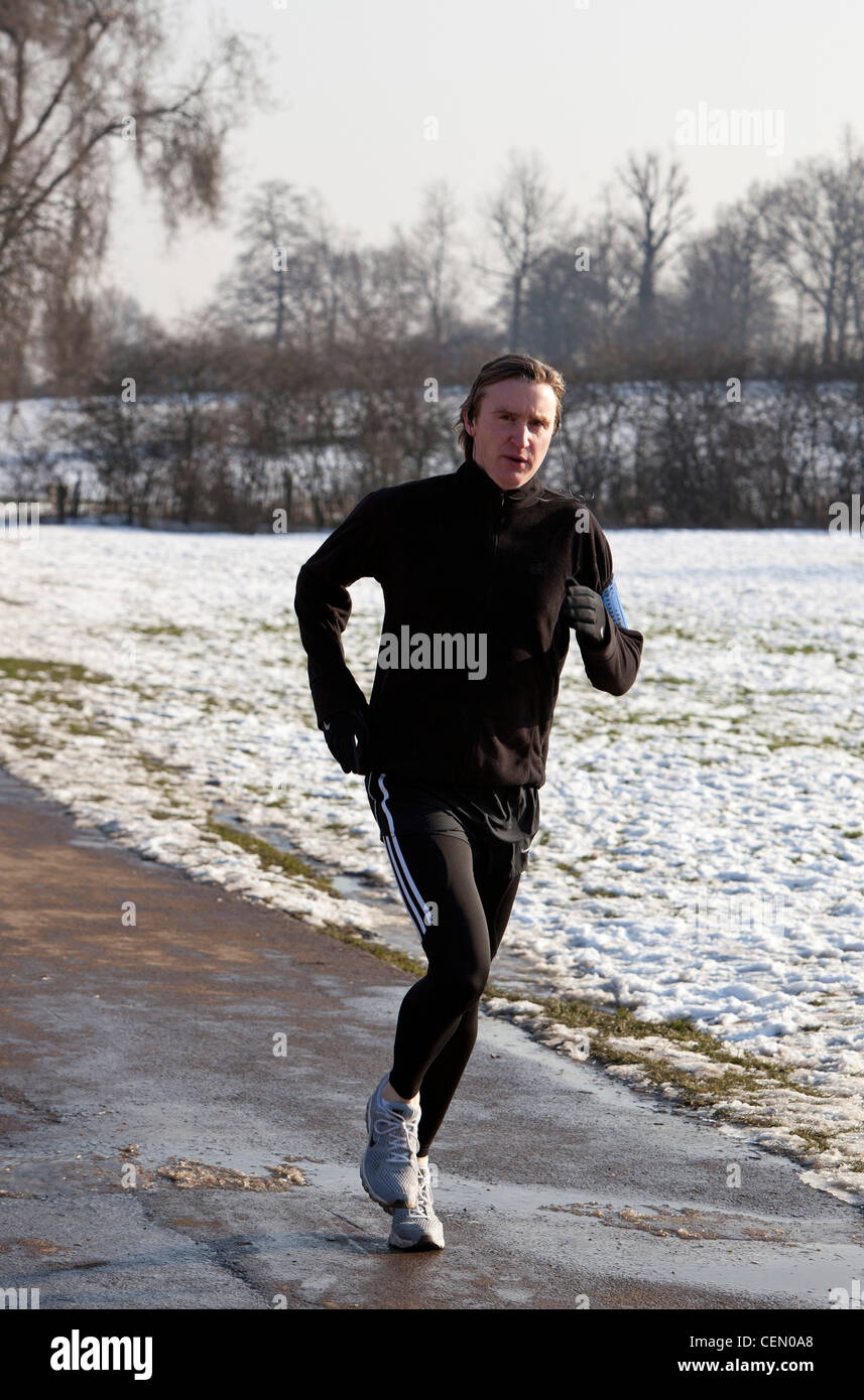 A piena lunghezza Ritratto di un uomo jogging su un asfalto sentiero in inverno, Hampstead Heath, London, England, Regno Unito Foto Stock