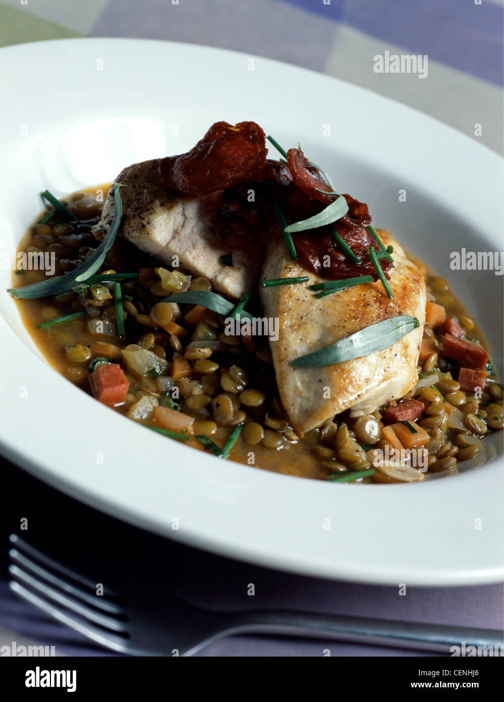 Pollo brasato di lenticchie: due filetti di pollo su lenticchie Chorizo salsiccia tagliata a fette in cima, cosparso di erba cipollina e il dragoncello erbe Foto Stock