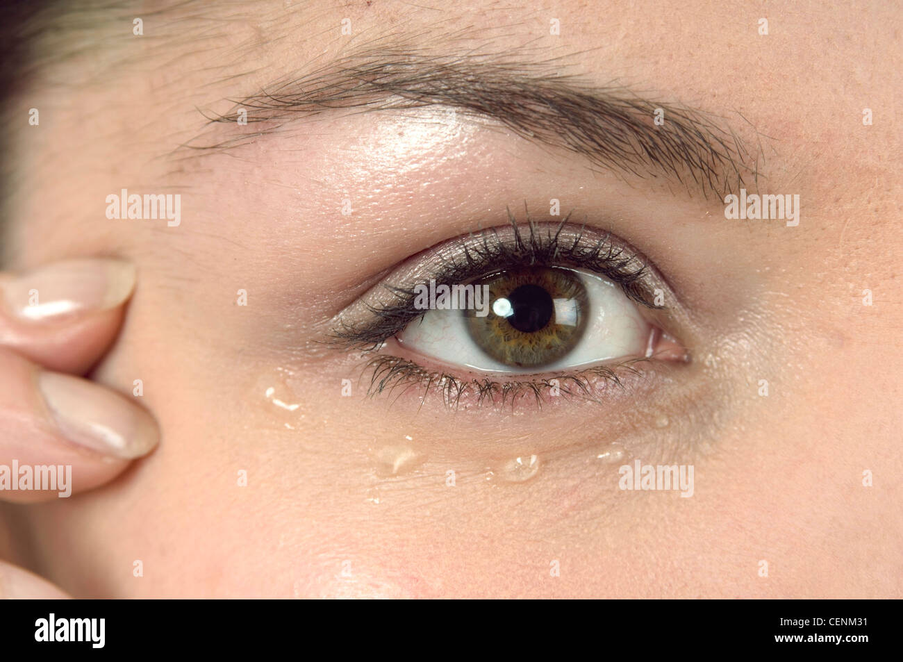 Ravvicinata di un occhio femminile con gel oculare sotto il coperchio inferiore e la punta delle dita in templi Foto Stock