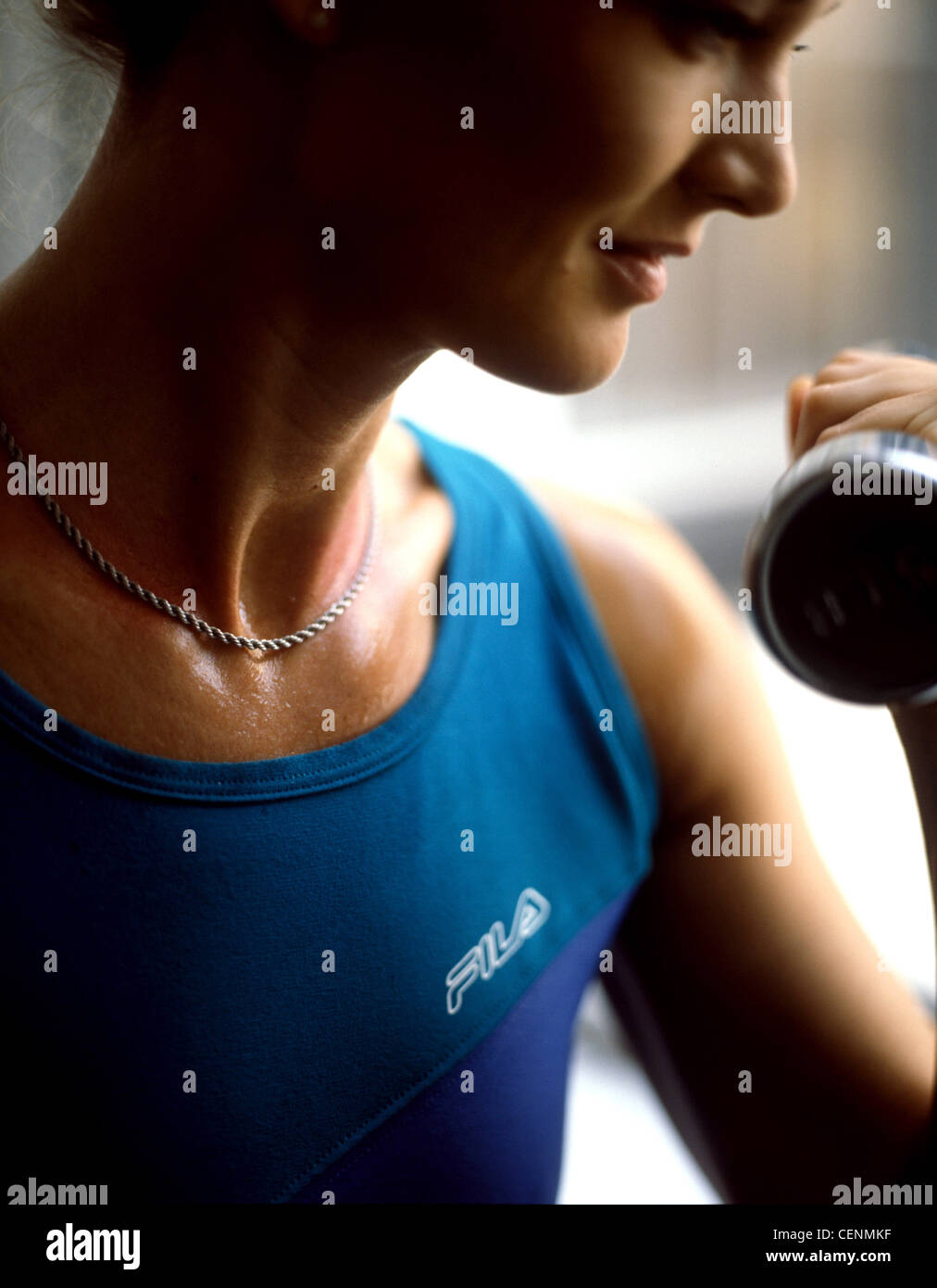 Immagine ritagliata della femmina, indossa una catena d'argento collana e giubbotto blu, esercitando con manubri, sorridente, guardando al lato Foto Stock