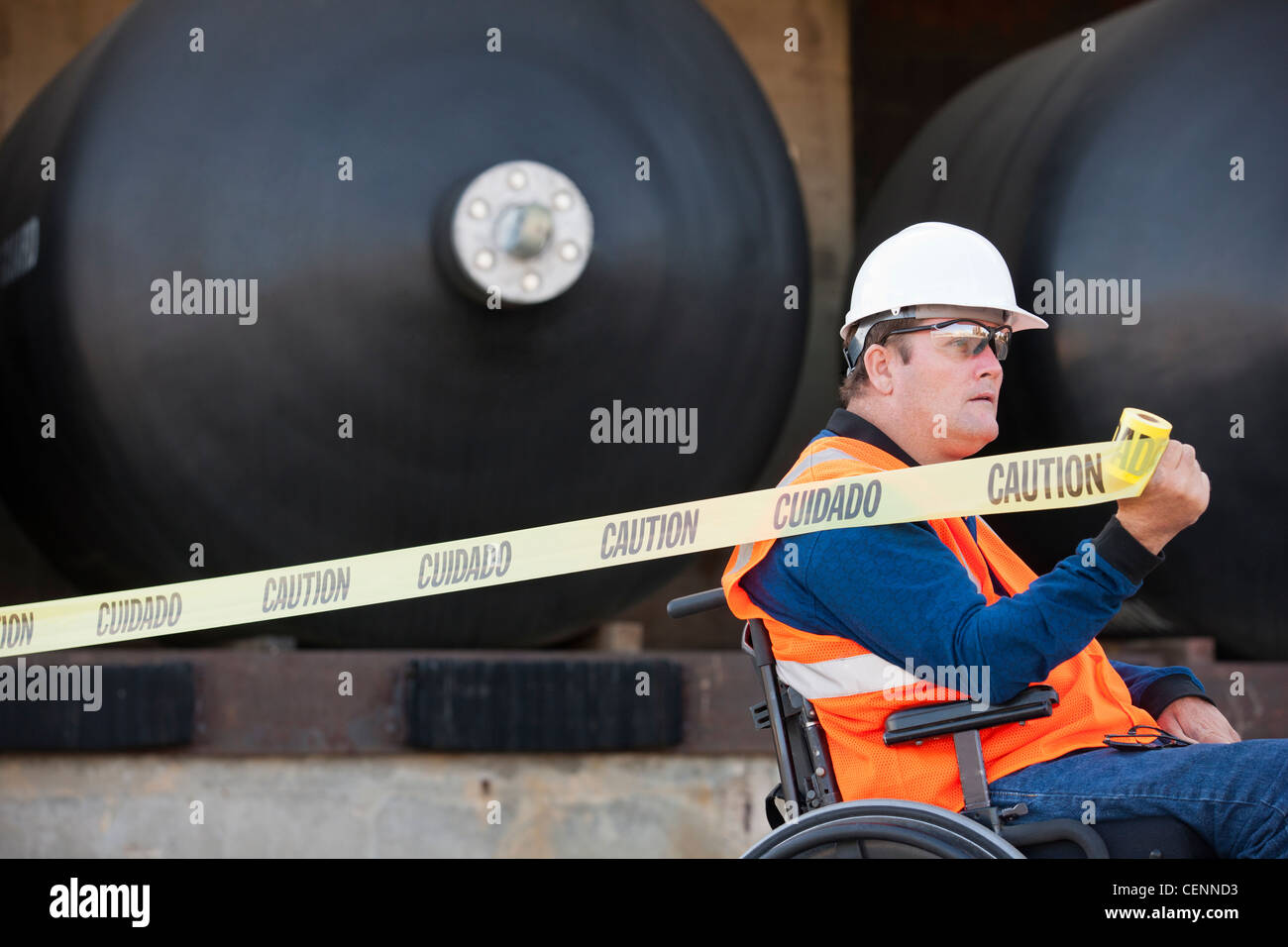 Facilities engineer in una sedia a rotelle tirando il nastro di attenzione nella parte anteriore del prodotto chimico dei serbatoi di stoccaggio Foto Stock