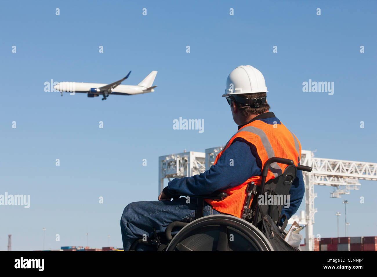 Ingegnere di trasporto in sedia a rotelle la visione di aereo di linea volare sopra i contenitori di spedizione e gru al porto Foto Stock