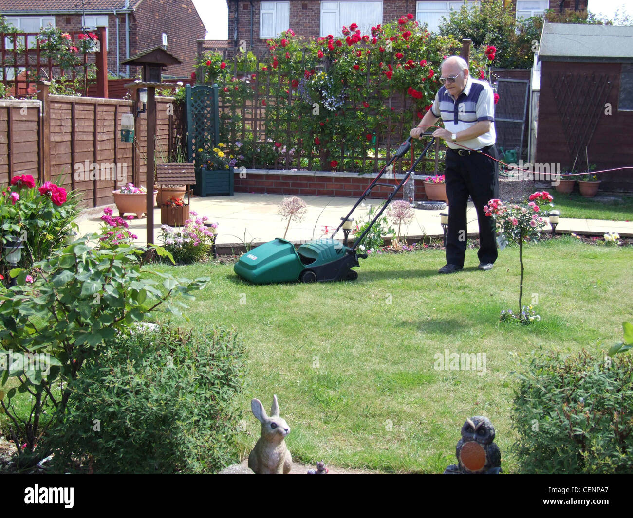 Maschio su 60 anni la falciatura di prato in un giardino con patio e un uccello tabella Foto Stock