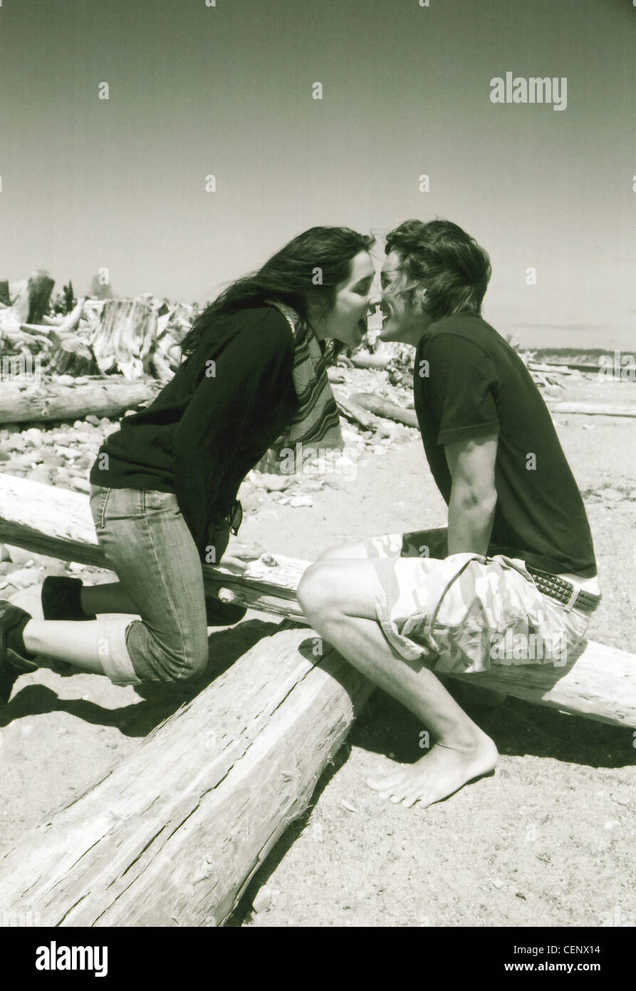 Immagine in bianco e nero di maschio e femmina seduto su altalena in legno sulla spiaggia proteso verso l'altra attorno al bacio Foto Stock