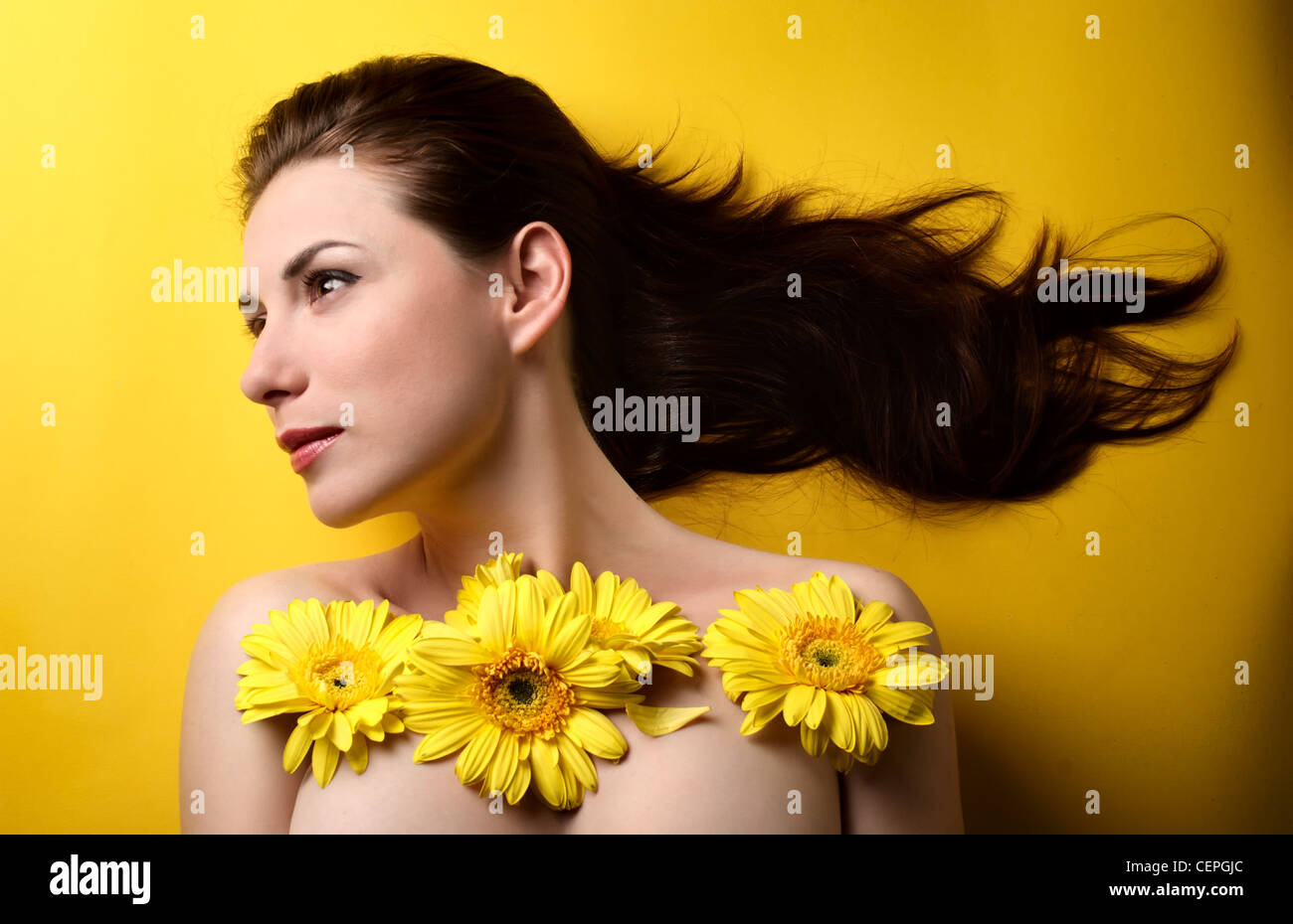 In Topless ritratto di una giovane e bella donna ricoperto di fiori gialli isolati su sfondo giallo Foto Stock