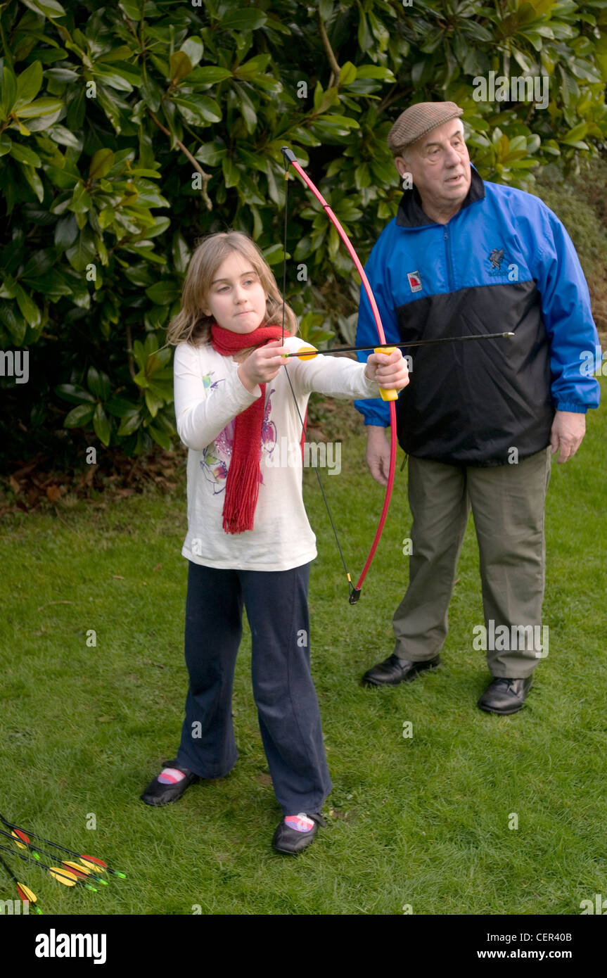 Un 9 anno vecchia ragazza gioca con un arco e frecce supervisionati da suo nonno Foto Stock
