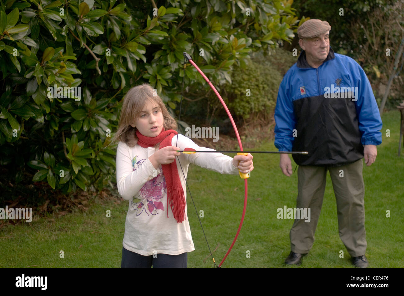 Un 9 anno vecchia ragazza gioca con un arco e frecce supervisionati da suo nonno Foto Stock