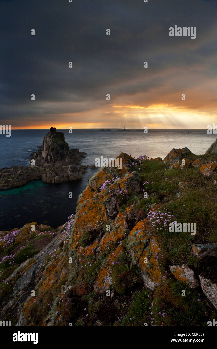 I raggi di luce solare attraverso la rottura di nuvole temporalesche su Longships Lighthouse, visto dal Land's End al tramonto. Foto Stock