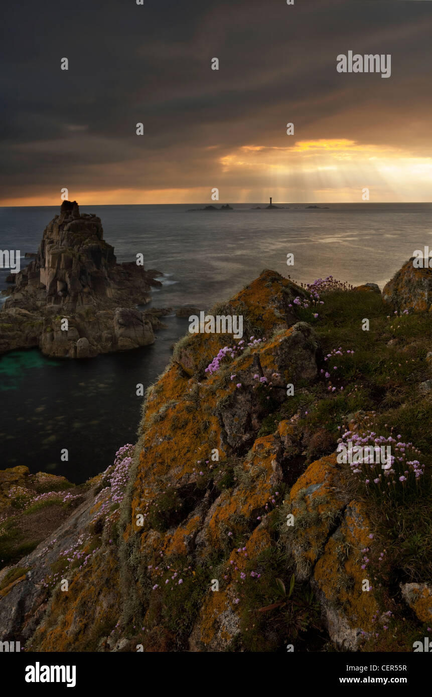 I raggi di luce solare attraverso la rottura di nuvole temporalesche su Longships Lighthouse, visto dal Land's End al tramonto. Foto Stock