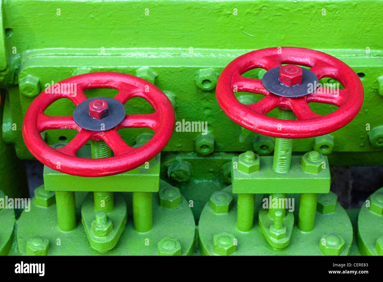 Ingegneria di due valvole di flusso con le maniglie verniciate in rosso contro il motore verniciato di verde Foto Stock