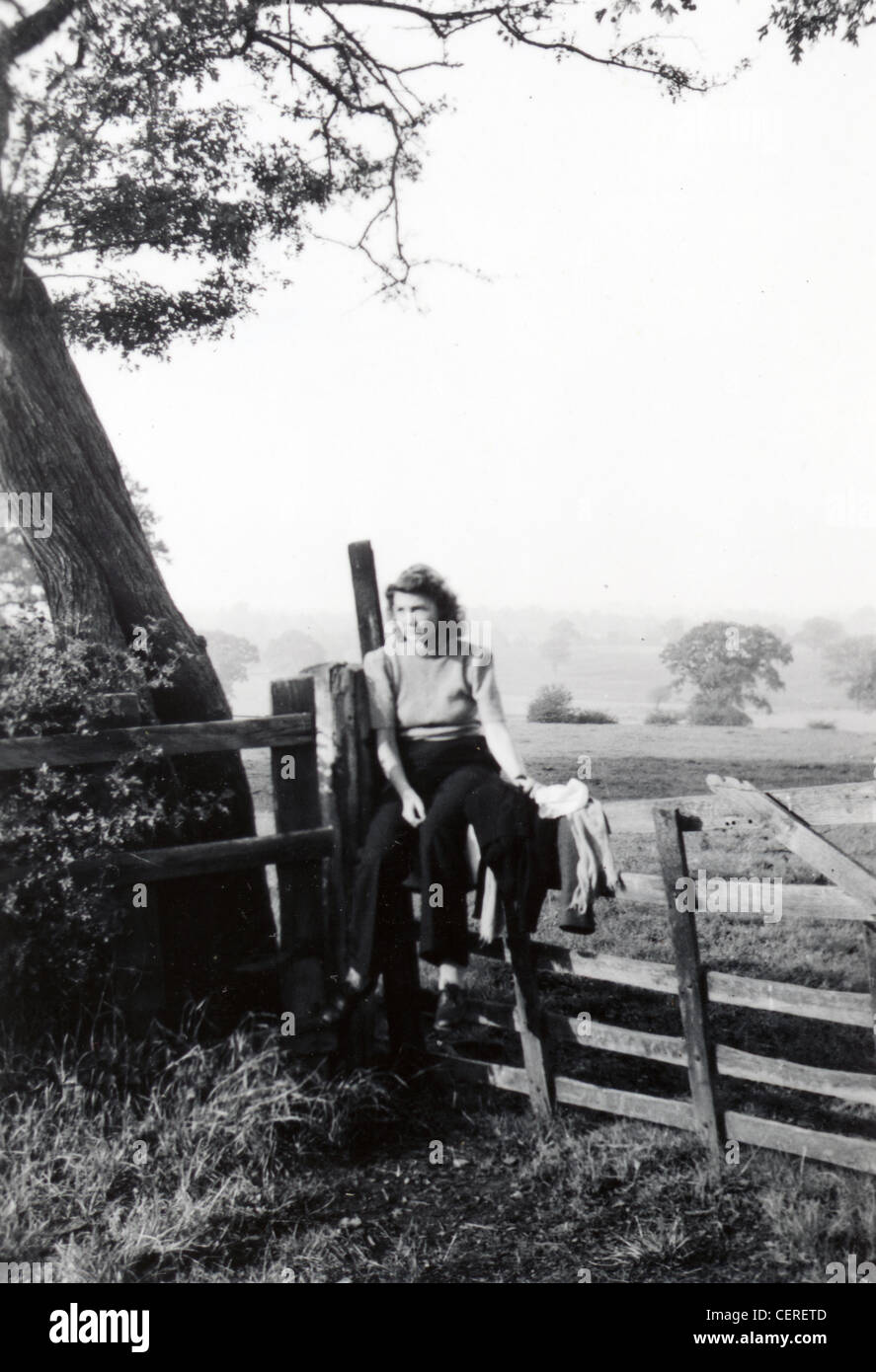 Giovane donna seduta su un cancello rurale mediante una struttura ad albero (C1945) Foto Stock