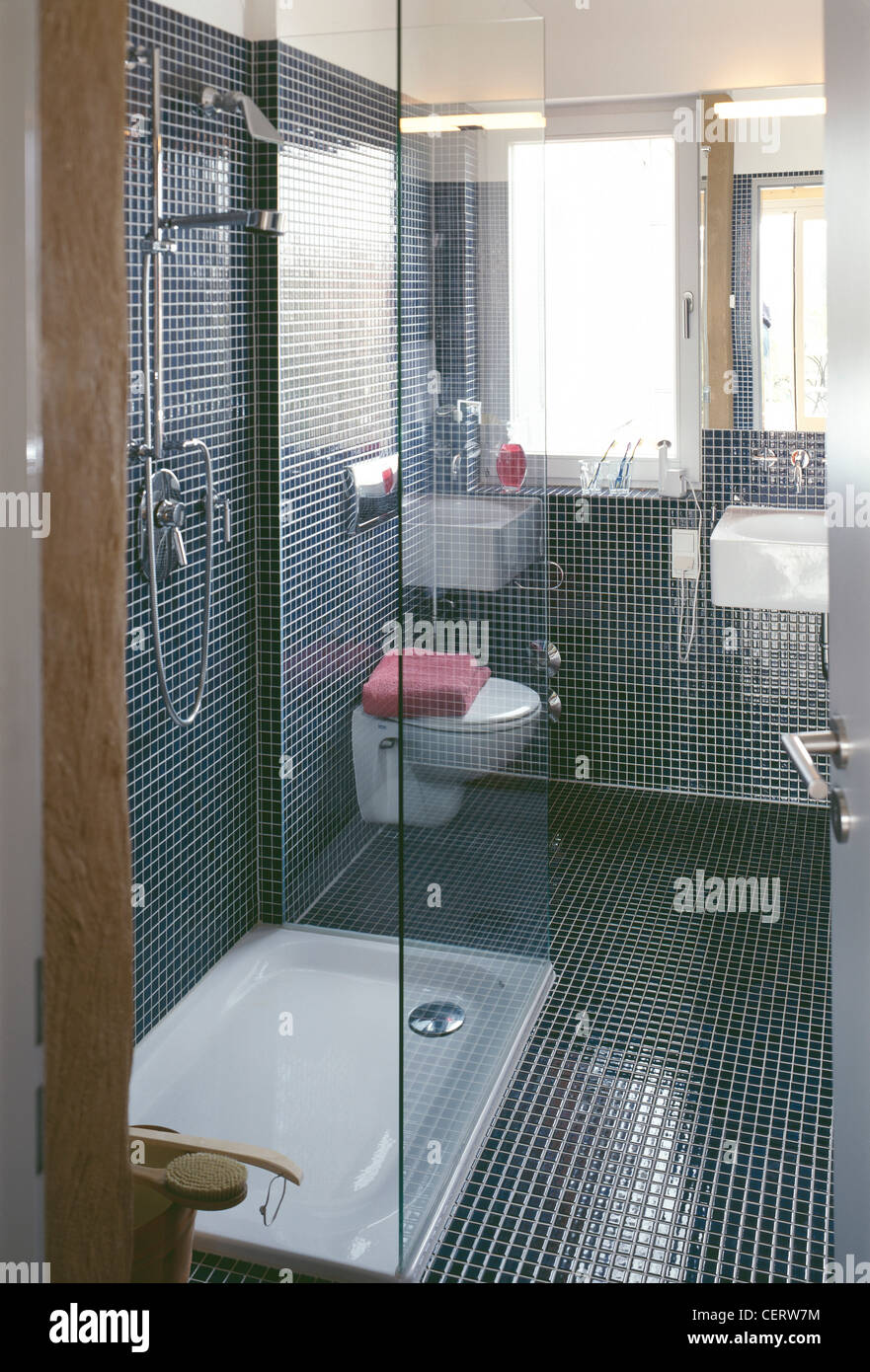 Stile moderno bagno rivestito di piastrelle a mosaico floand pareti, box doccia vassoio bianco e lo schermo di vetro, doccia cromo, bianco e wc Foto Stock