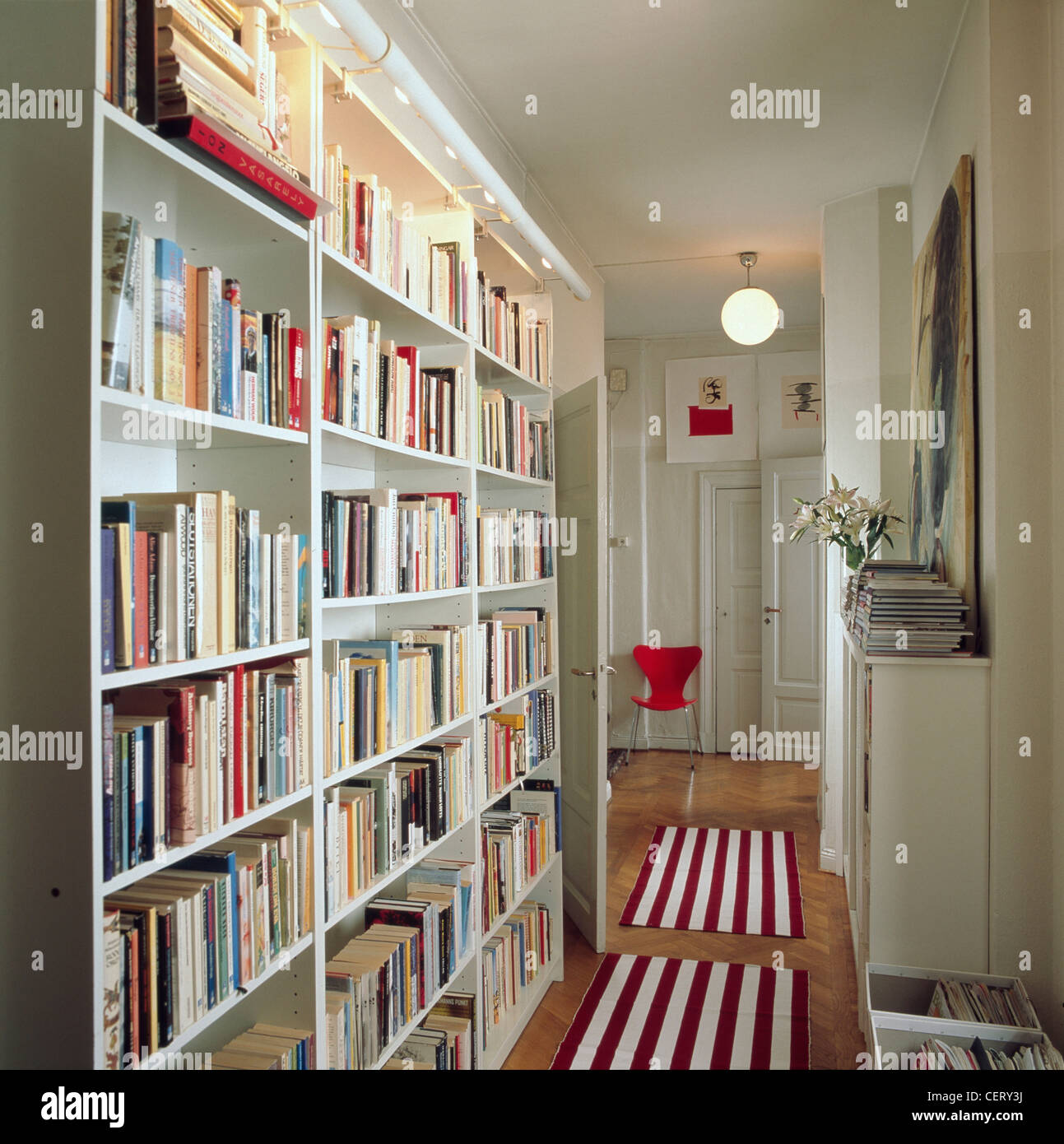 Corridoio con il bianco libreria lungo una parete, pavimento in parquet e rossa e bianca a strisce di tappeti magazine Foto Stock