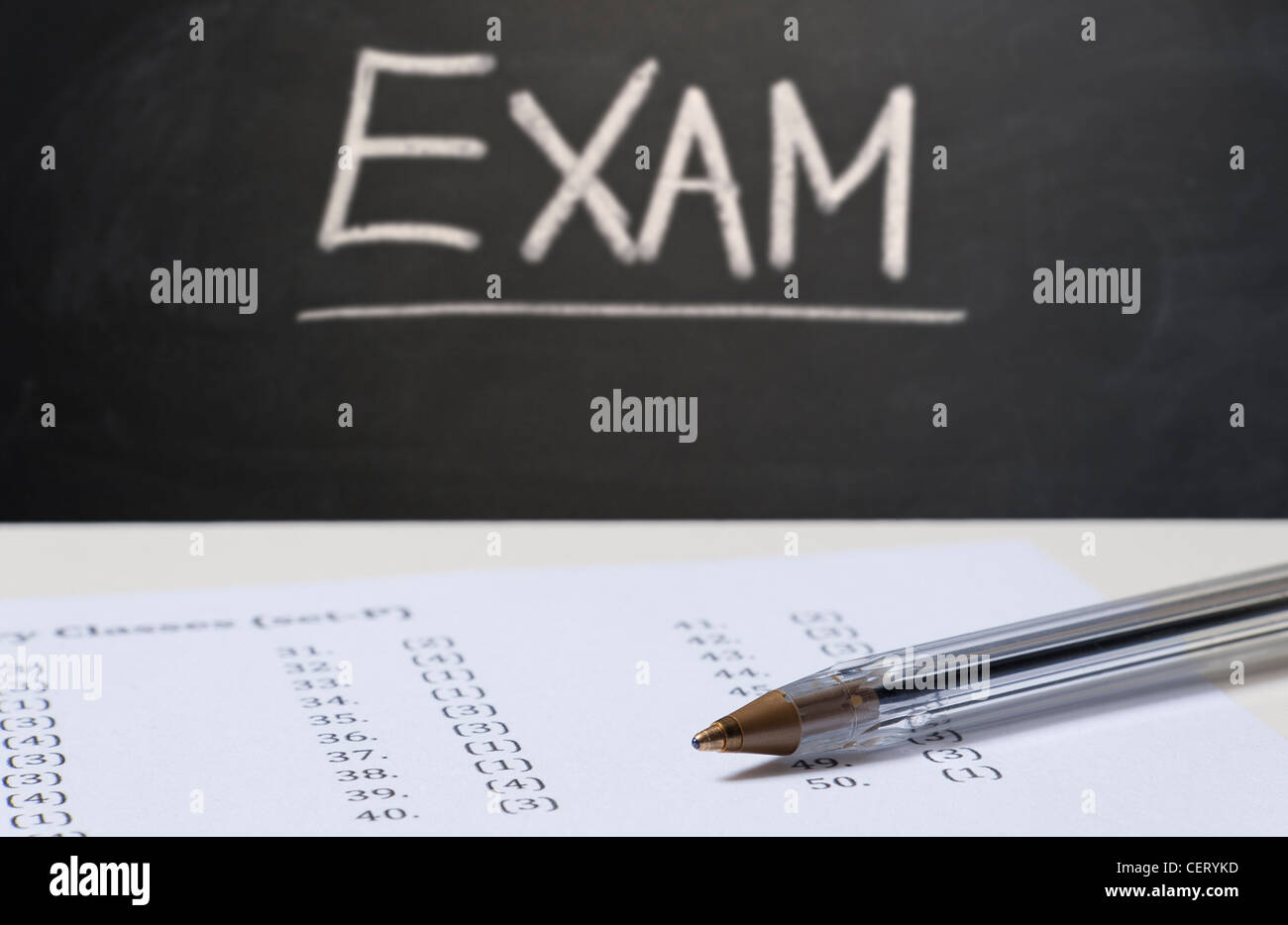 Close up on an exam paper and a pen with a blackboard in the background with EXAM written in chalk Foto Stock