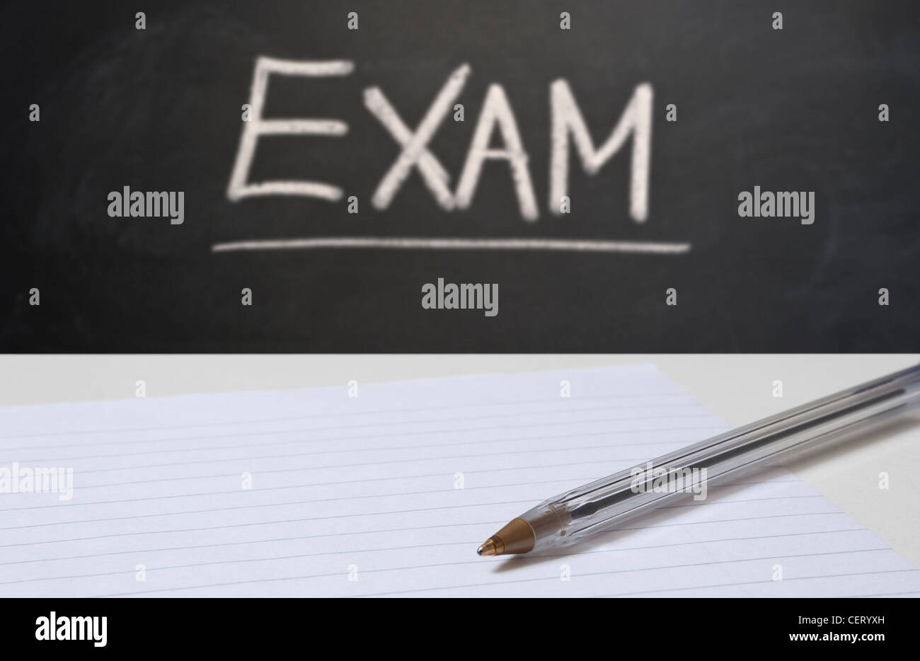 Close up on blank paper and a pen with a blackboard in the background with EXAM written in chalk Foto Stock
