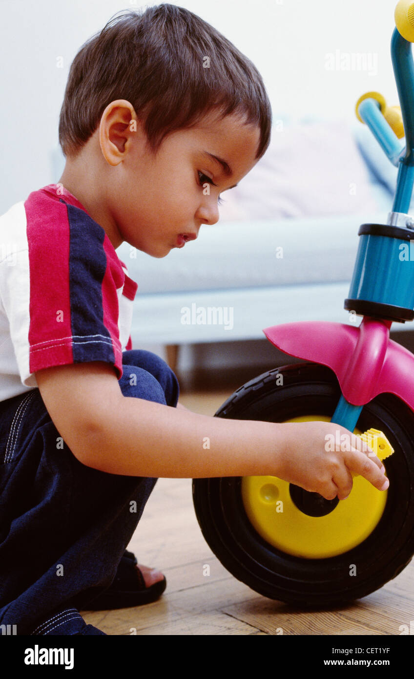 Bimbi maschio brunette, indossando il bianco e il rosso di t-shirt e jeans, seduta con la ruota anteriore del triciclo, controllo pedali Ian Foto Stock