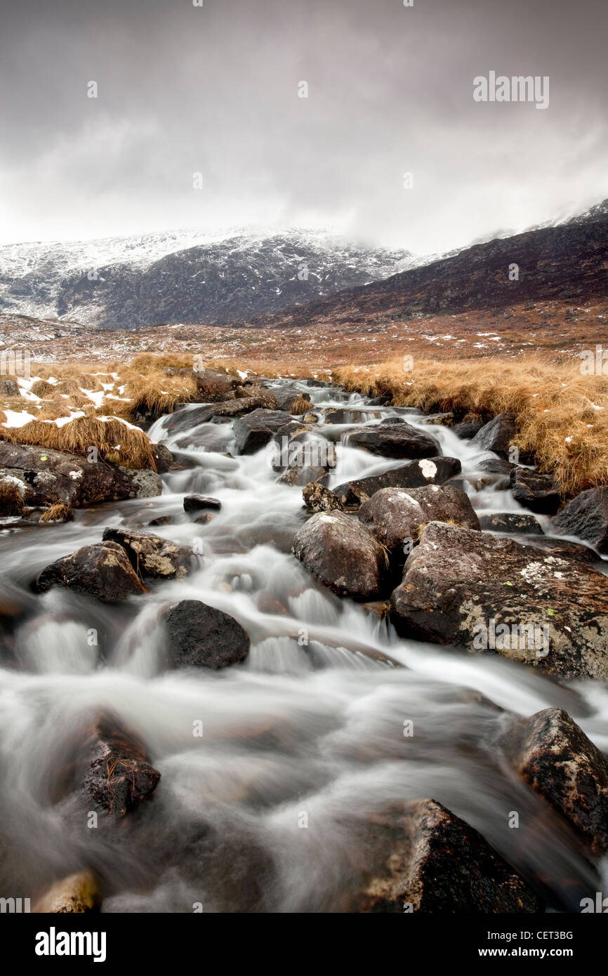 L'acqua che scorre verso il basso dalla montagna su rocce nel Parco Nazionale di Snowdonia in inverno. Foto Stock