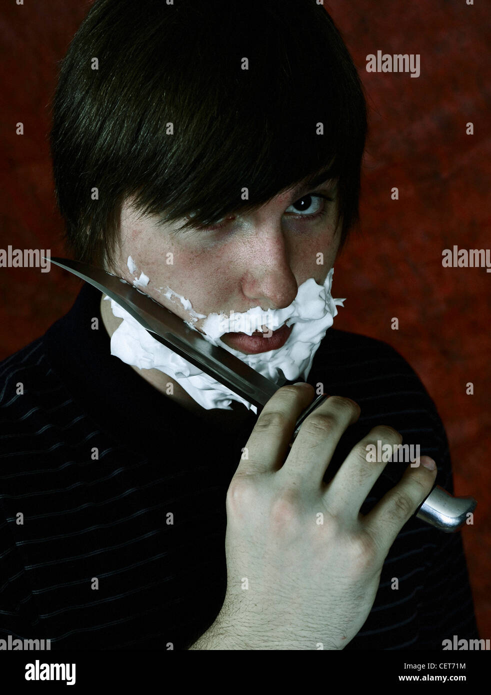 Un giovane uomo la rasatura il viso con un coltello Foto Stock