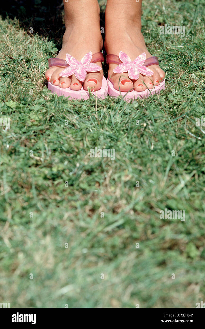 Femmina ritagliate le caviglie e i piedi indossando rosa flip flop con fiore sequined e rosso smalto per unghie sulla toenails Foto Stock
