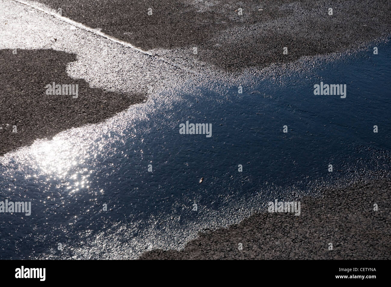 La riflessione del sole in una pozzanghera sulla strada Foto Stock