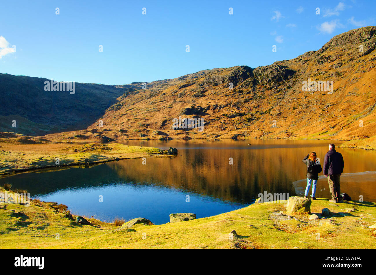 Walkers accanto parzialmente congelato Easedale Tarn vicino a Grasmere nel Lake District inglese Foto Stock