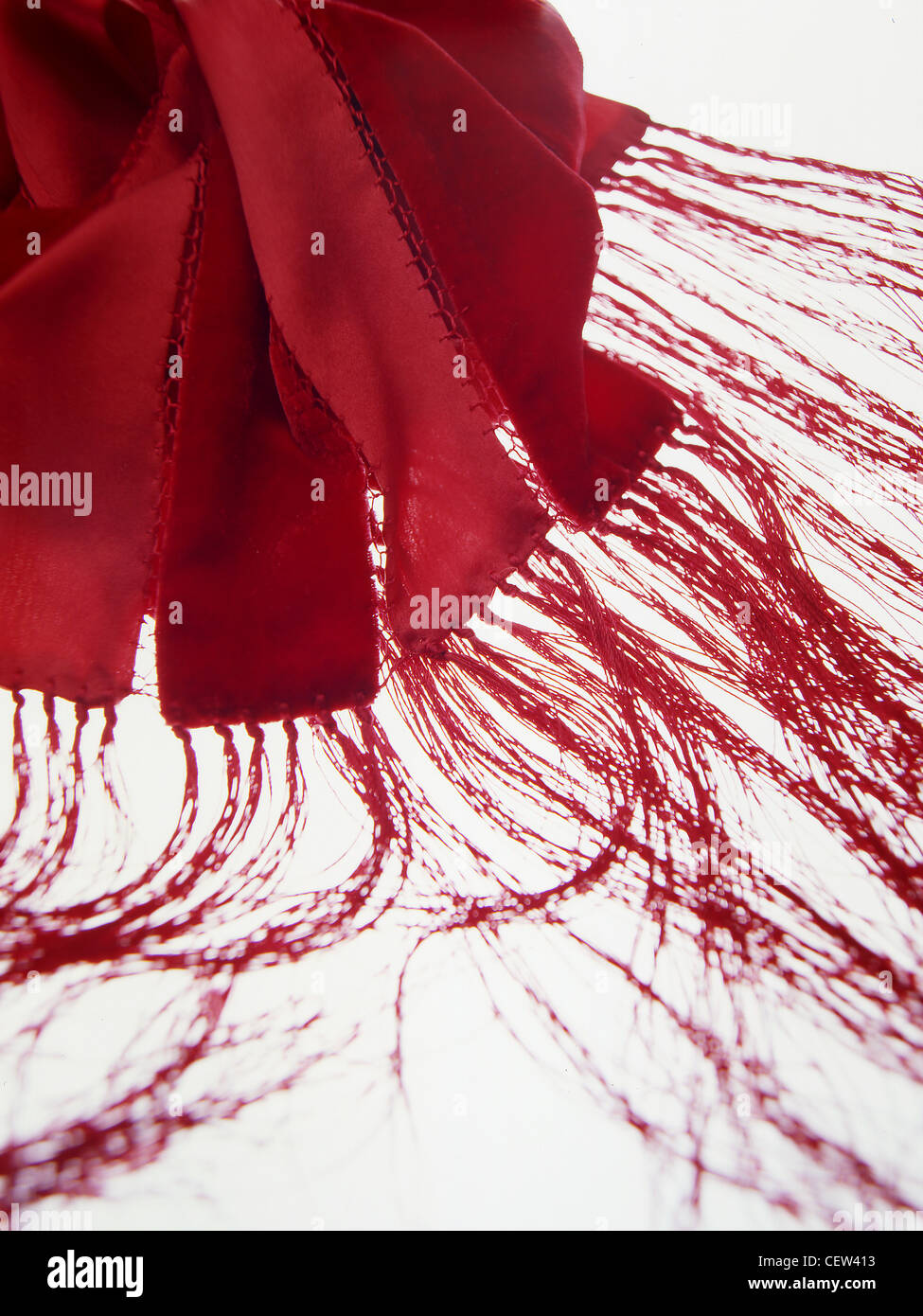 Primo piano, dettaglio astratto di una sciarpa o scialle con frange rosse, che mostra fibre tessili fluide e bordi di tessuto cuciti su uno sfondo bianco brillante, Foto Stock