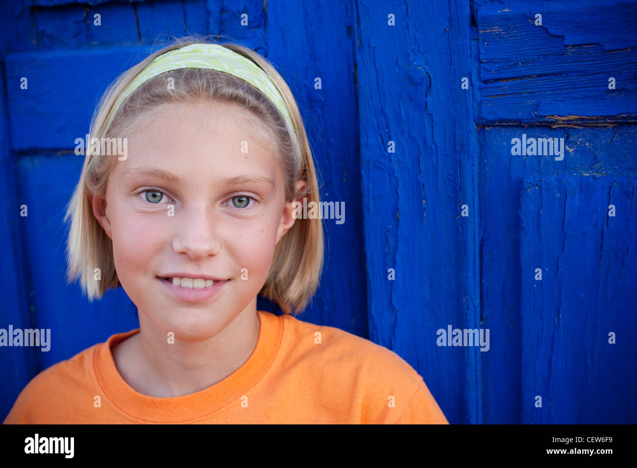 9 anno vecchia ragazza che indossa la fascia che si trova di fronte un blu brillante porta sorridente. Foto Stock