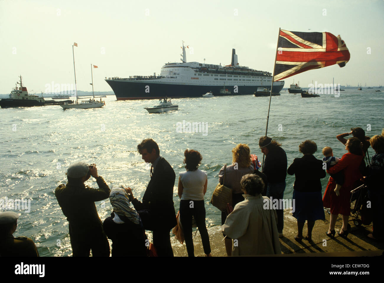 Nave Queen Elizabeth 2. QE2 salpa per la Guerra delle Falkland del 1981. Familiari e amici mandano loro lungo la strada una grande bandiera britannica Union Jack e una flottiglia di piccole imbarcazioni li mandano sulla portaerei di truppe in viaggio. Maggio 1982 1980 UK HOMER SYKES Foto Stock