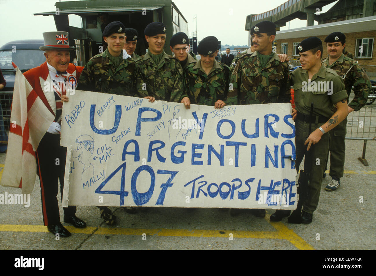 I soldati britannici della Guerra delle Falklands aspettano di partire da Southampton sulla QE2 con mascotte che porta una bandiera di croce rossa di San Giorgio su sfondo bianco e che indossa un cappello. Circa maggio 1982. Soldati che tengono uno striscione, su le vostre truppe argentine 407 qui. Facevano parte del "407 Road Transport Troop", il Royal Corps of Transport. 1980s Regno Unito. HOMER SYKES Foto Stock