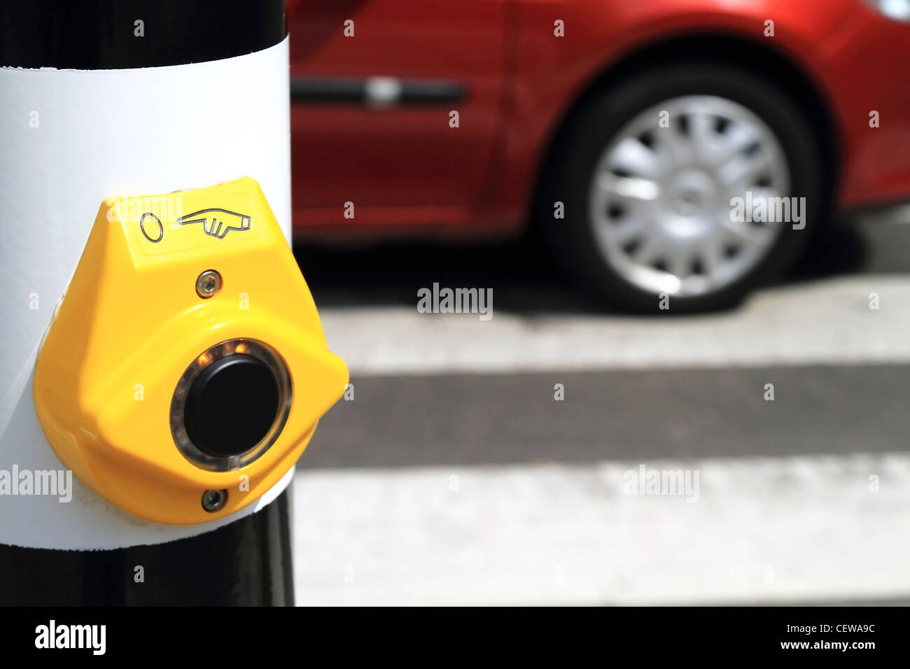 Immagine ravvicinata di un giallo crosswalk pulsante con una vettura sfocata e la strada in background Foto Stock