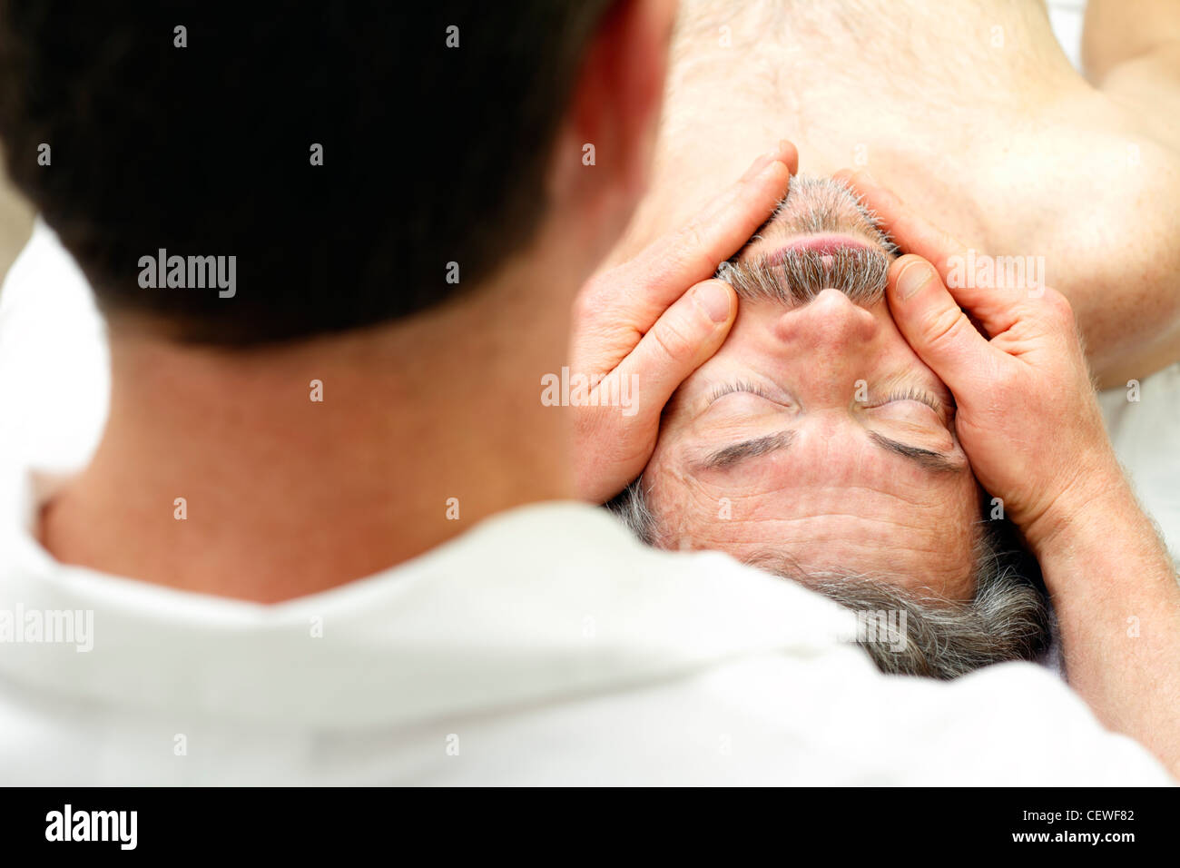 Terapista del massaggio massaggio del viso di un uomo che stabilisce a faccia in su sul tavolo. Uomo maturo ottenendo faccia massaggiato da un maschio terapista di massaggio a un sano spa. Foto Stock