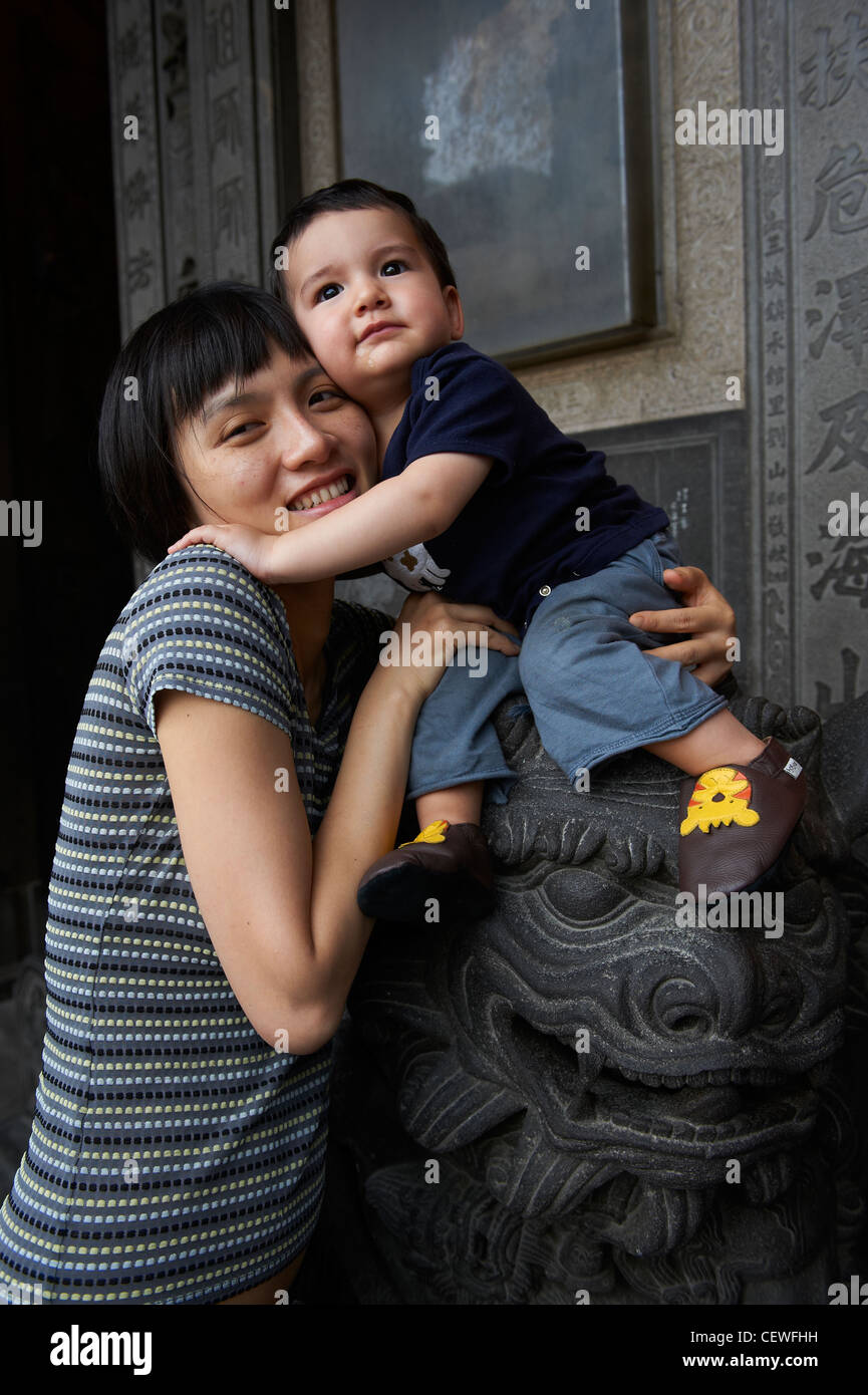 Una madre con il suo giovane figlio seduto sulla cima di un cinese Lion statua. Foto Stock