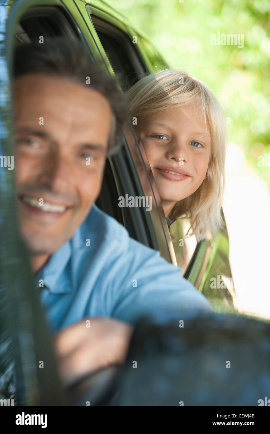 Ragazzo di equitazione in auto con il padre, sporgersi finestra e sorridente in telecamera Foto Stock