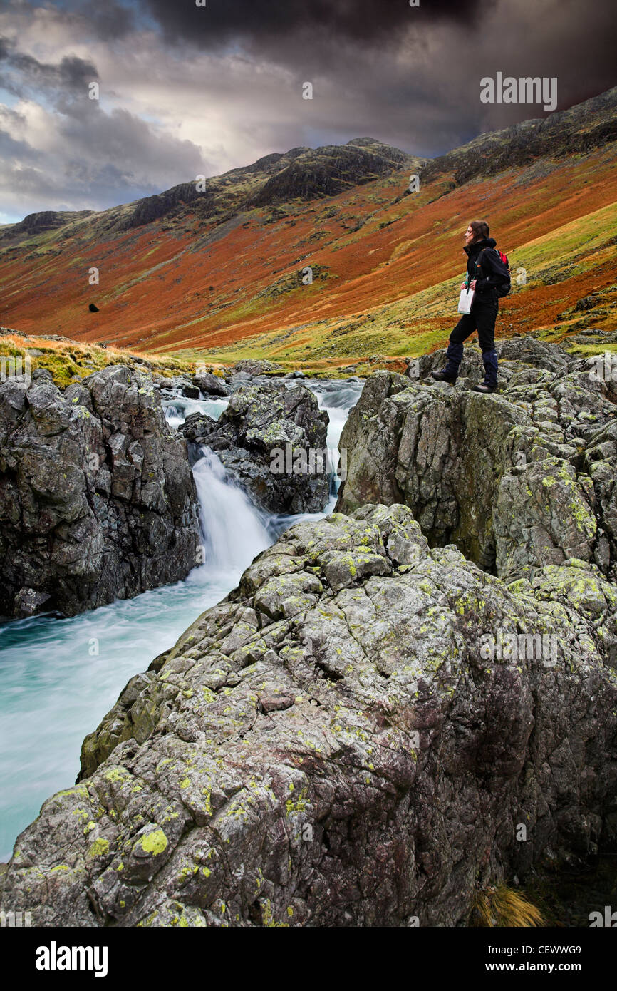 Giovane donna in piedi su massi vicino al fiume Esk. Il fiume Esk inizia nel grande Moss sotto Scafell Pike in inglese Lak Foto Stock