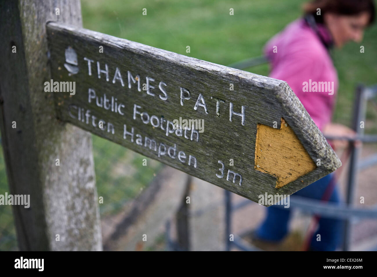 Un viandante con il suo cane passando attraverso un cancello al di sotto di un cartello sulla Thames Path che mostra la direzione e il chilometraggio di Clifton Foto Stock