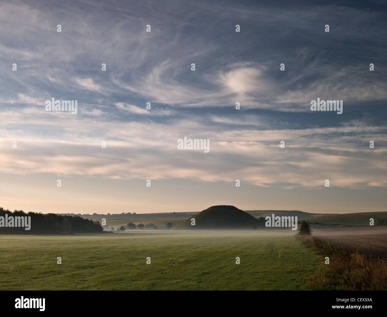 Vista su campo nebbioso di Silbury Hill, il più alto preistoria umana fatta a tumulo in Europa, sotto le nuvole di vorticazione. Foto Stock