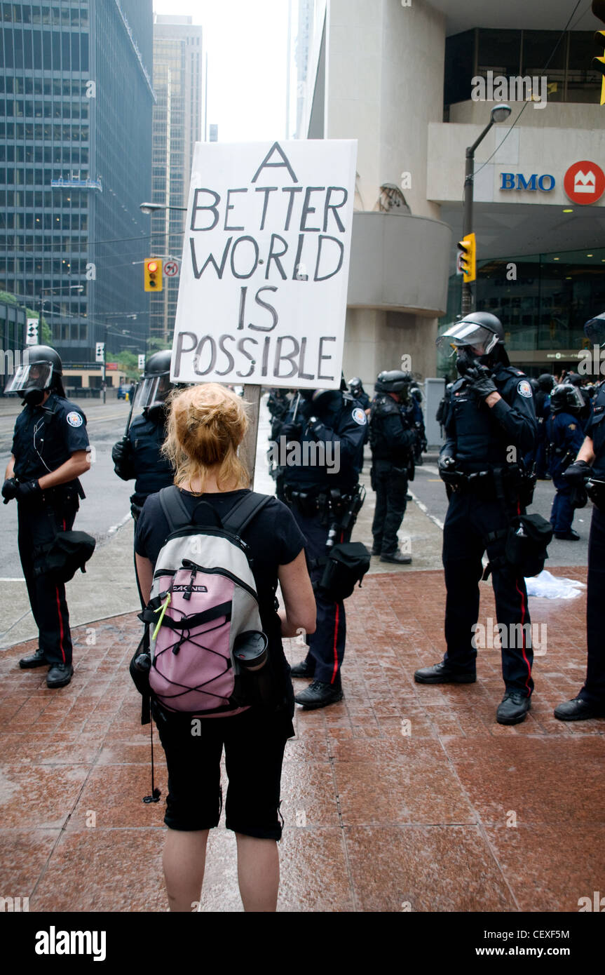 Un giovane manifestante femmina tenendo in mano un cartello davanti a Toronto la polizia antisommossa durante il Vertice del G20 a Toronto, Ontario, Canada, nell'estate del 2010. Foto Stock