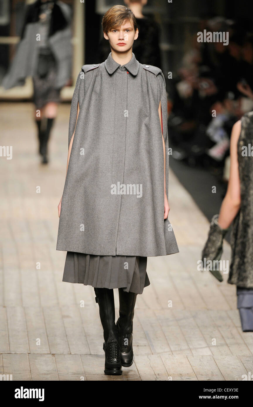 Antonio Marras Milano pronto a indossare in autunno e inverno grigio lunghezza al ginocchio cape coat con slitsarms, grigio gonna plissettata e stivali neri Foto Stock