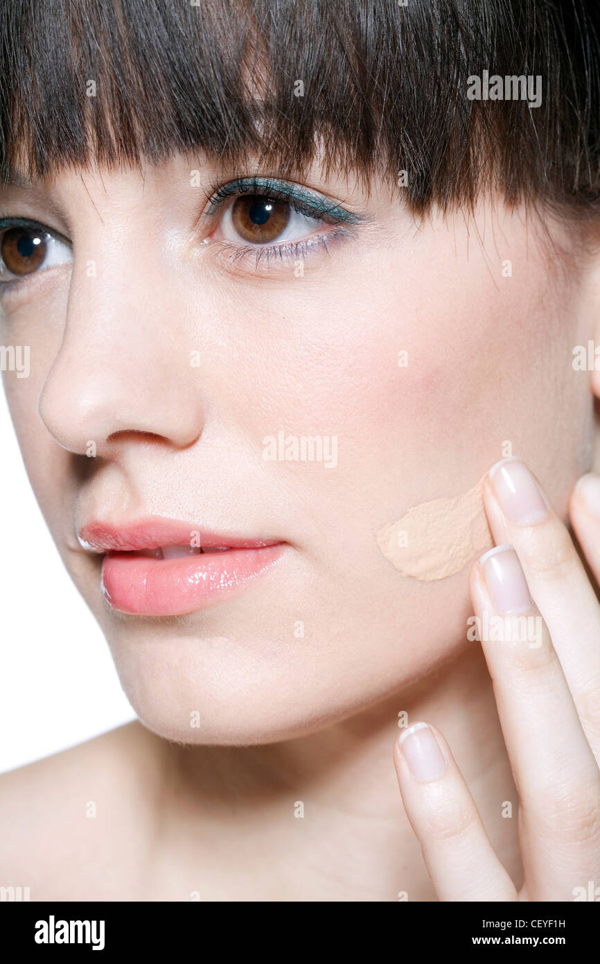 Femmina di frange brunette legati i capelli sul retro, applicando fondotinta liquido alla sua guancia le punte delle sue dita, c'erano pochi sorrisi, Foto Stock
