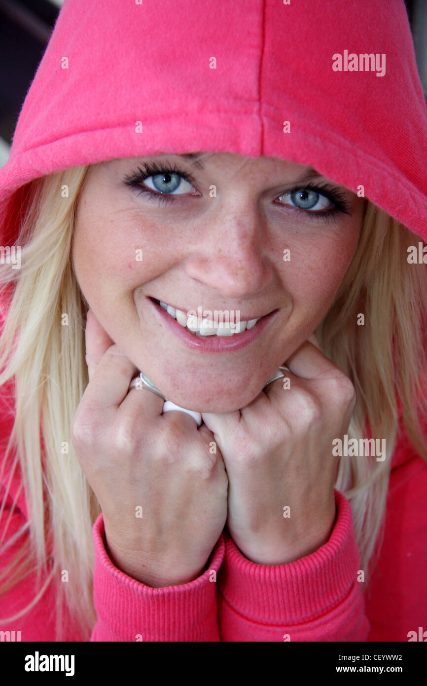 Donna che indossa un rosa luminoso incappucciati ponticello, con il cofano sollevato, sorridente alla telecamera appoggiato il suo mento sul suo knuckles Foto Stock