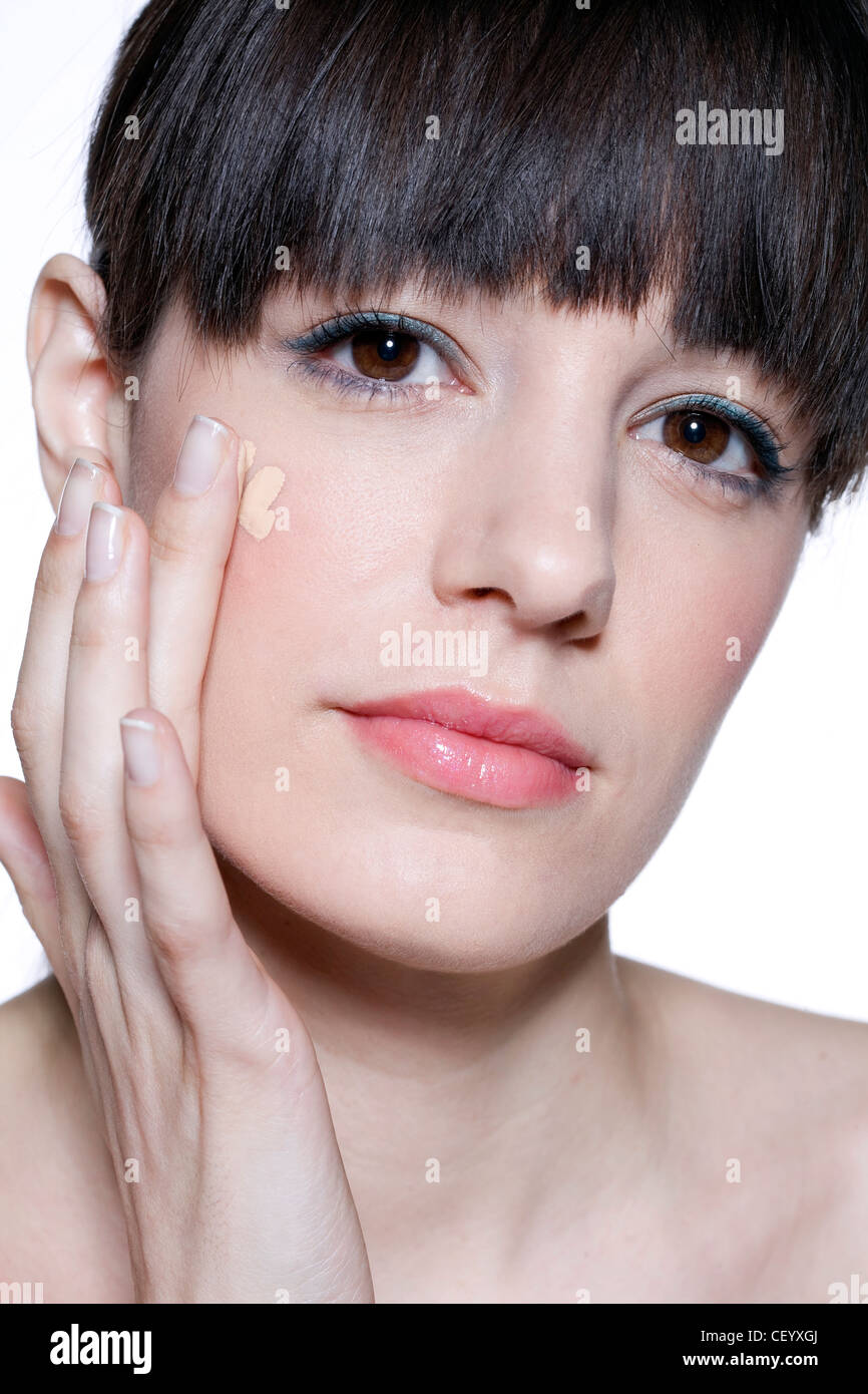 Femmina di frange brunette legati i capelli sul retro, applicando fondotinta liquido alla sua guancia le punte delle sue dita, c'erano pochi sorrisi, Foto Stock