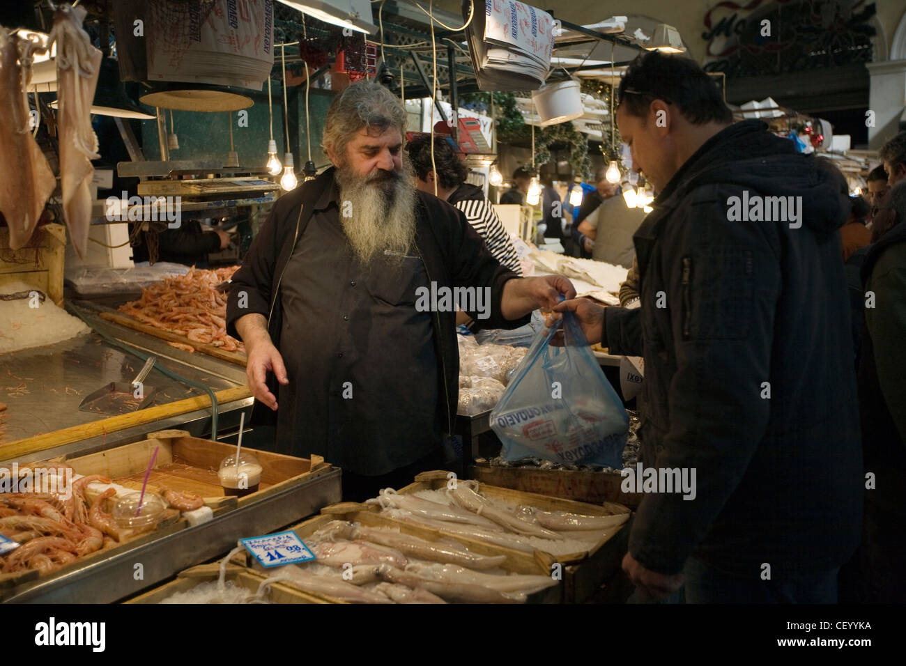Un pescivendolo serve un cliente al suo in stallo il mercato centrale di Atene su Athinas Street. Atene, Grecia Foto Stock